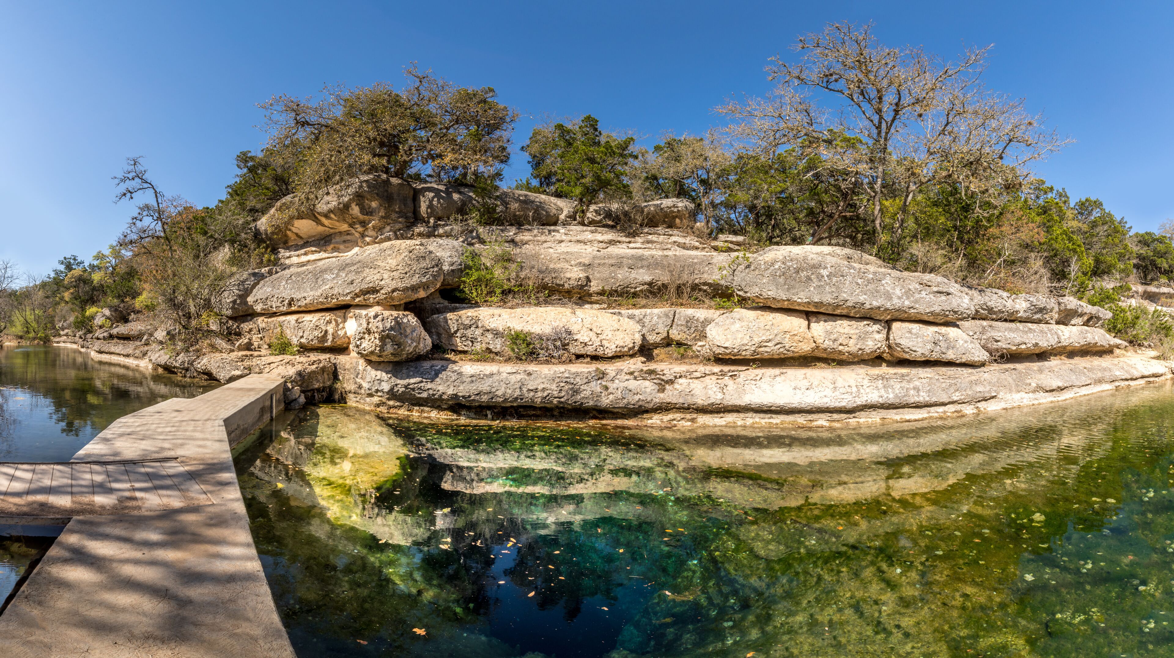 A rocky island with a clear pool of water reflecting the sky and surrounding trees.