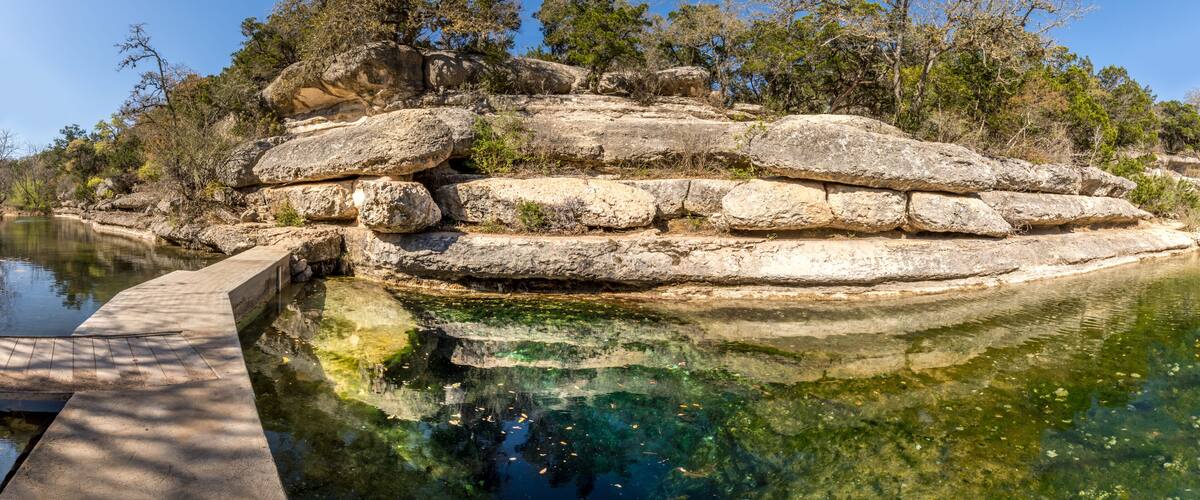 A rocky island with a clear pool of water reflecting the sky and surrounding trees.
