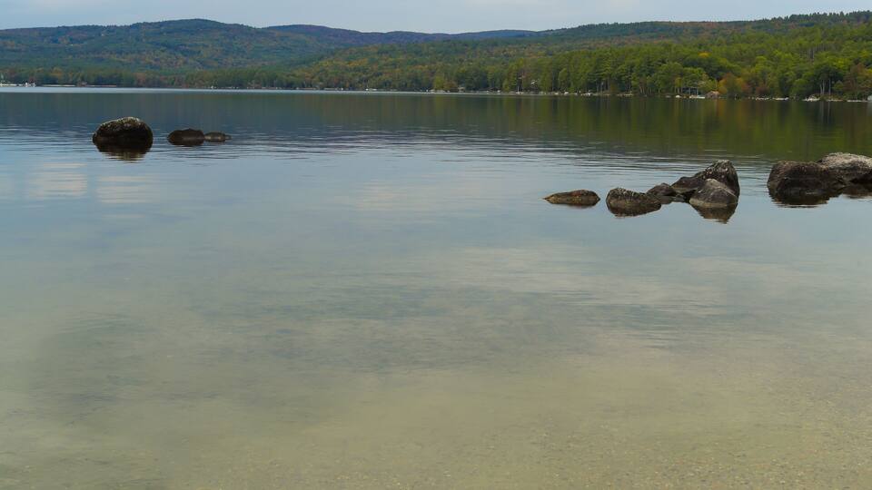 A calm lake with clear water, surrounded by hills and trees.
