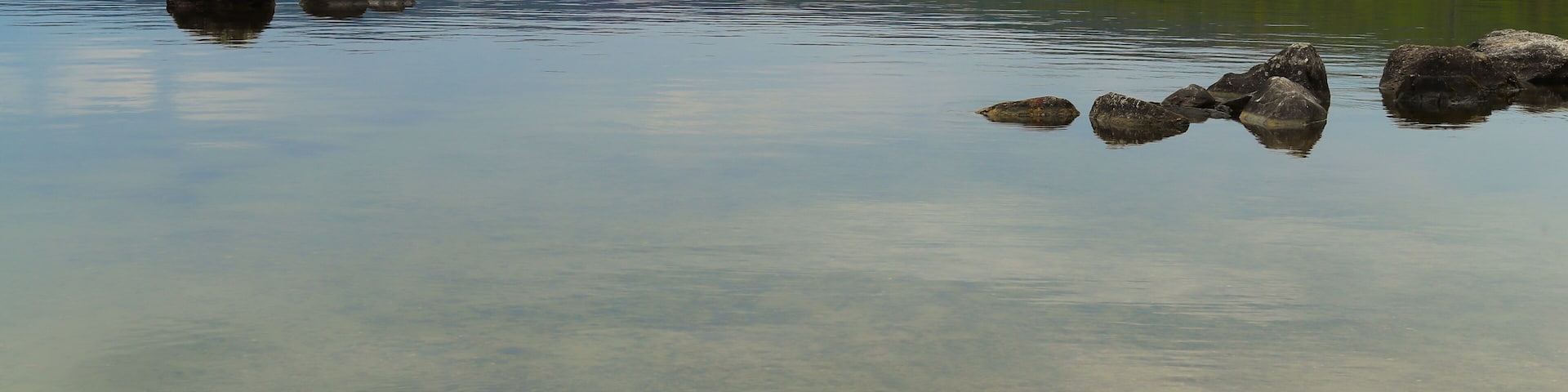 A calm lake with clear water, surrounded by hills and trees.