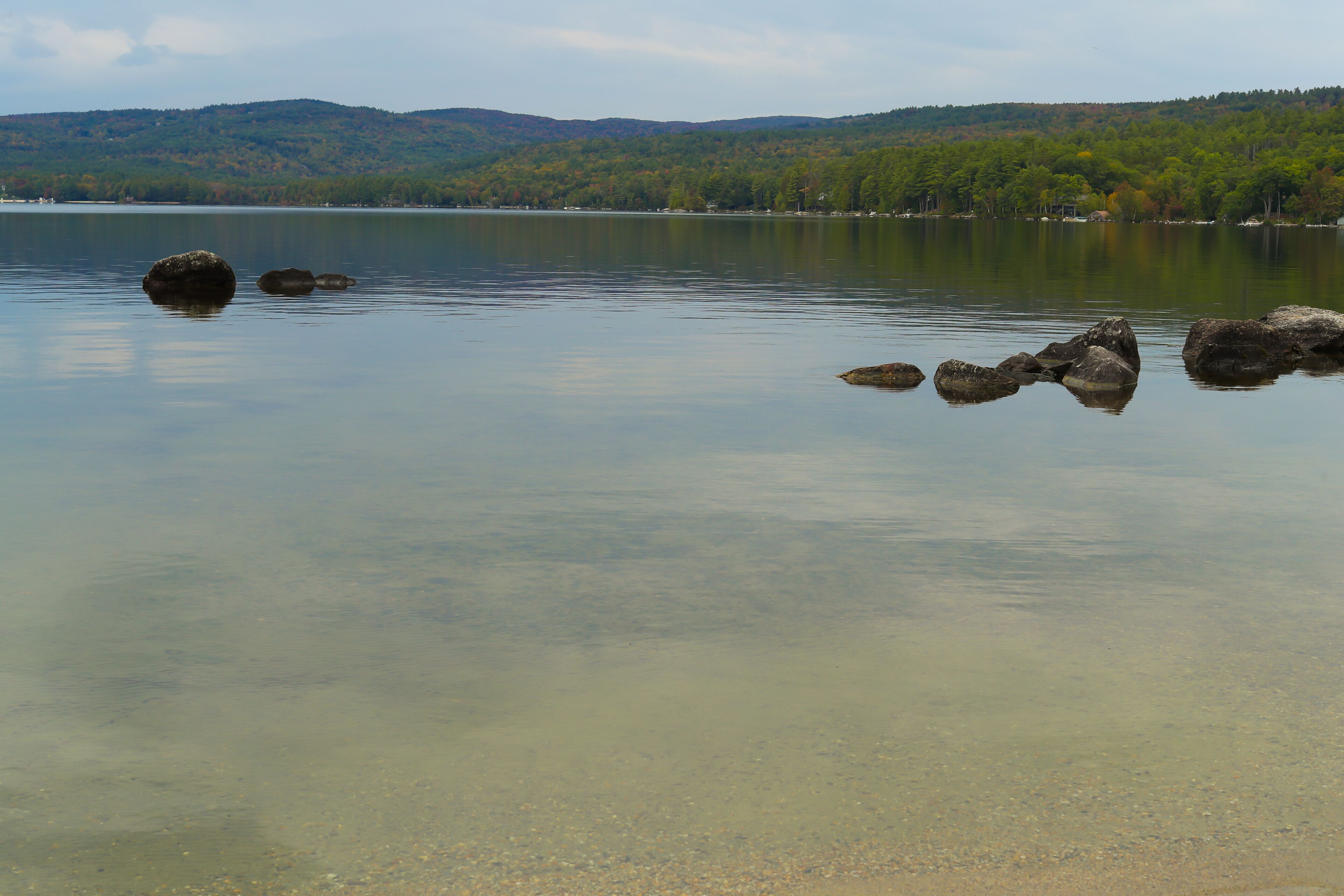 A calm lake with clear water, surrounded by hills and trees.