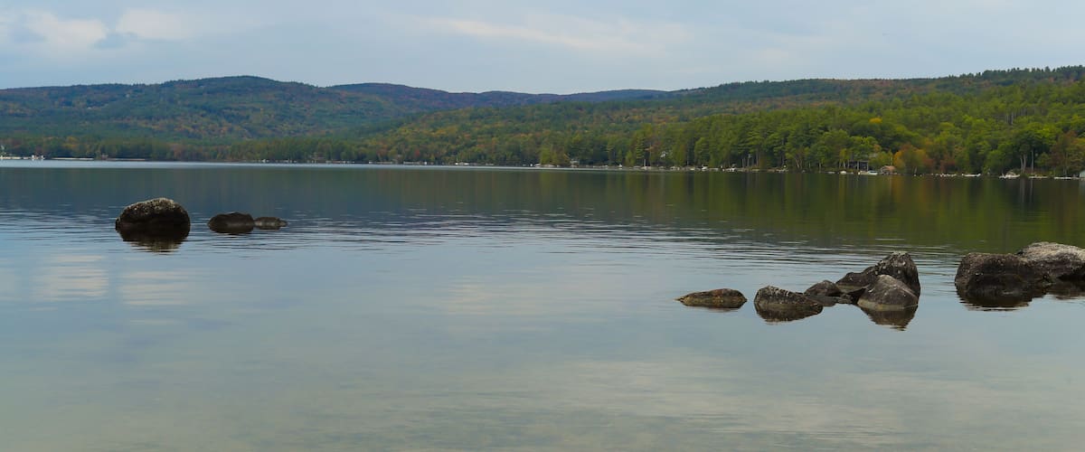 A calm lake with clear water, surrounded by hills and trees.