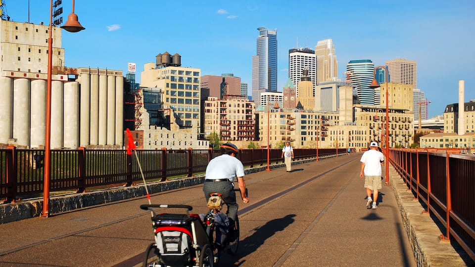 A pedestrian bridge with a city skyline in the background, featuring modern and historic buildings.