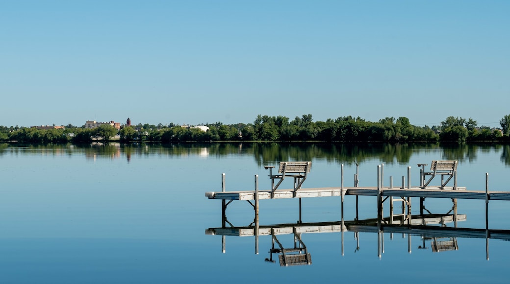 An inviting boat dock is reflected in the glassy water of Lake Irving, the first lake on the Mississippi river, with Bemidji, Minnesota, the 2018 Best Town in Minnesota, seen across the lake.