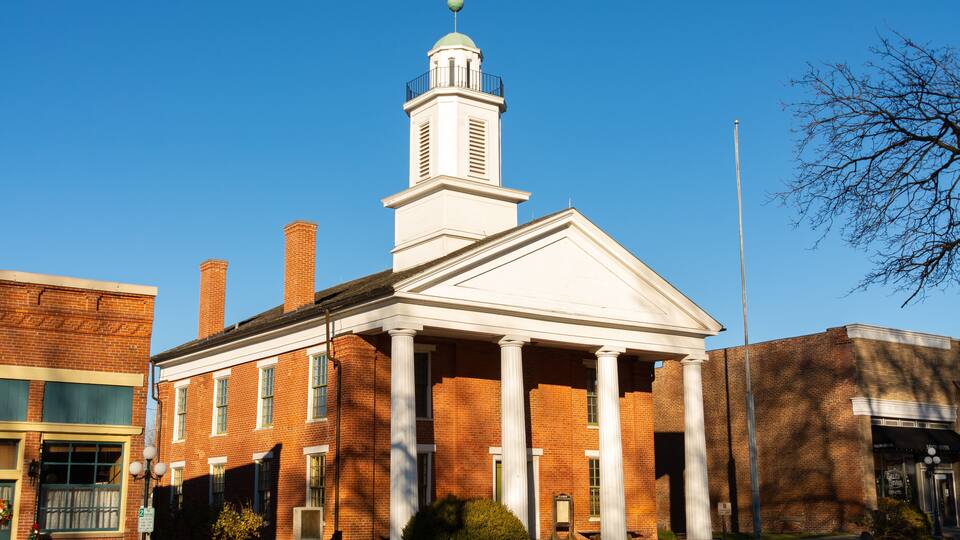A brick building with a white pediment and columns, a clock tower, and a flagpole.