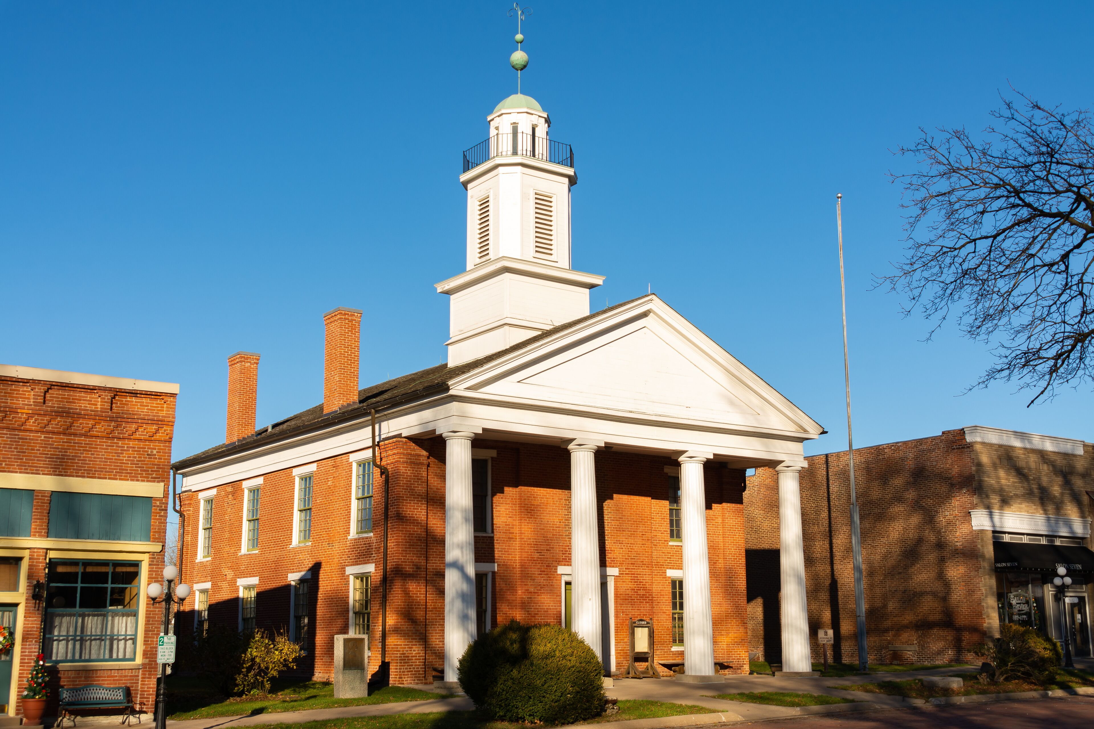 A brick building with a white pediment and columns, a clock tower, and a flagpole.