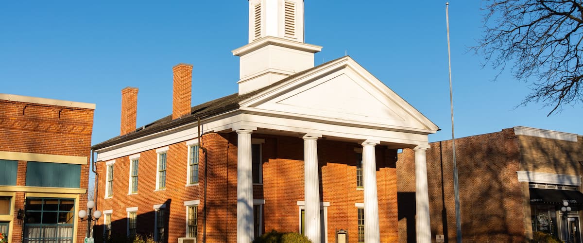 A brick building with a white pediment and columns, a clock tower, and a flagpole.