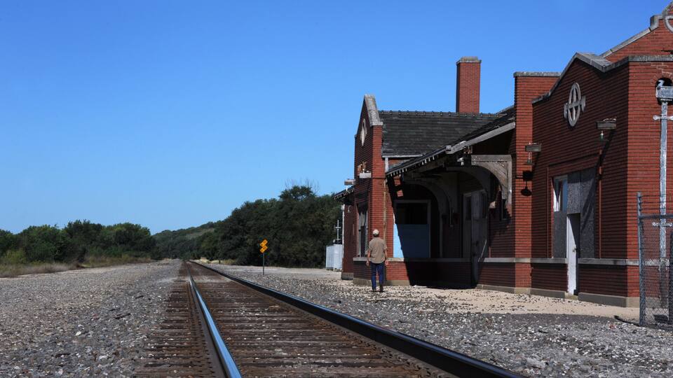 A railway track leading to a brick building with a clock tower.