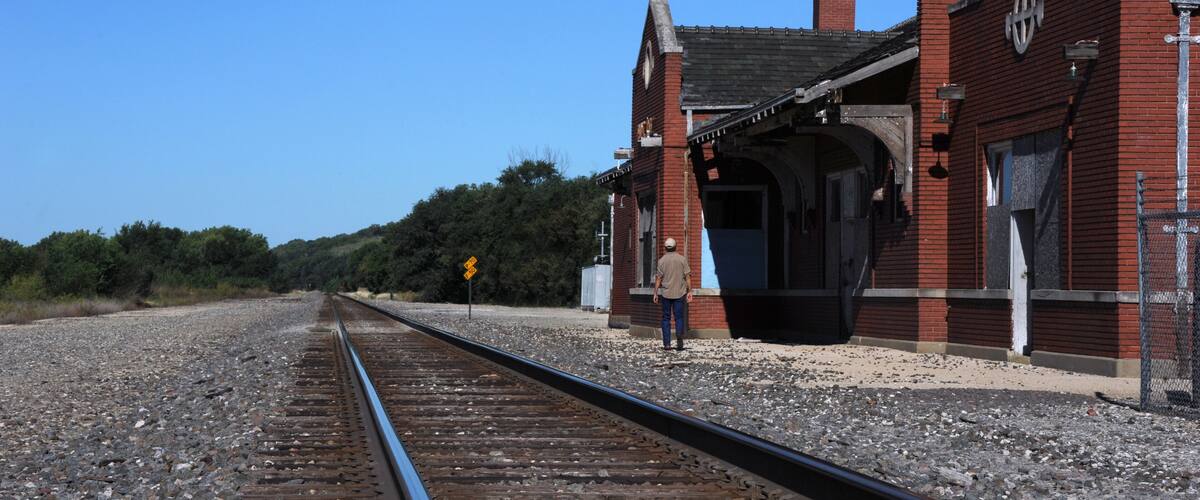 A railway track leading to a brick building with a clock tower.