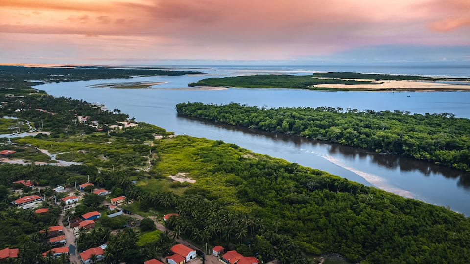 A river winding through a lush landscape with dense greenery and small houses with red roofs.