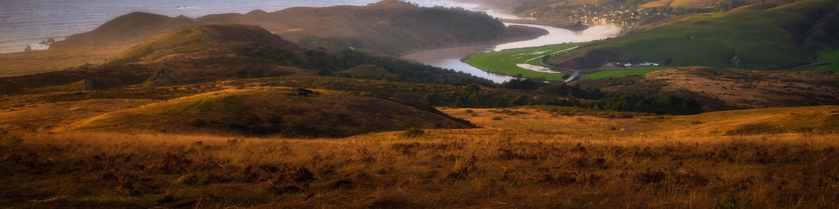 A coastal landscape with rolling hills, a river, and a distant shoreline.