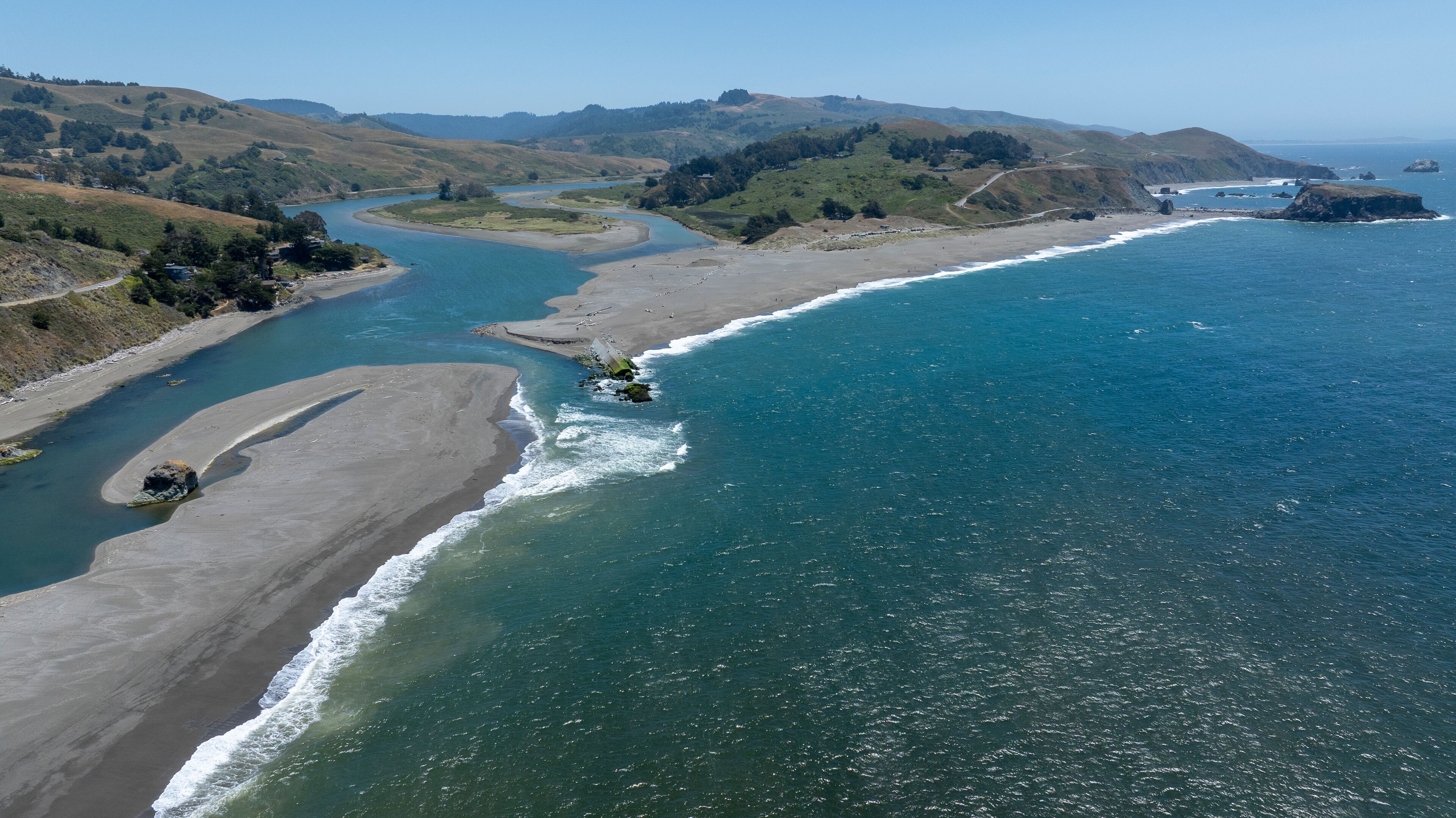 A coastal landscape with a river, beach, and hills.