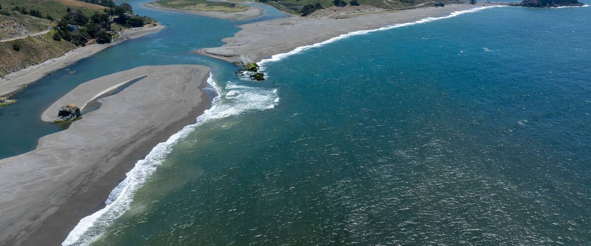 A coastal landscape with a river, beach, and hills.