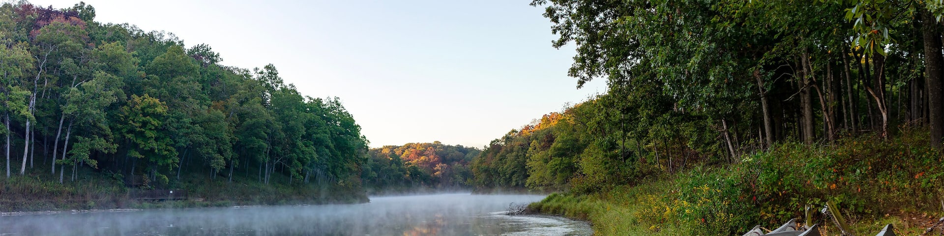 A calm river with canoes lined up on the bank, surrounded by dense forest.