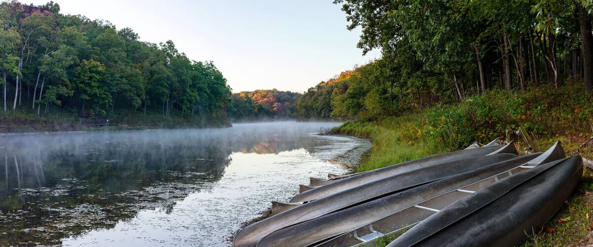 A calm river with canoes lined up on the bank, surrounded by dense forest.