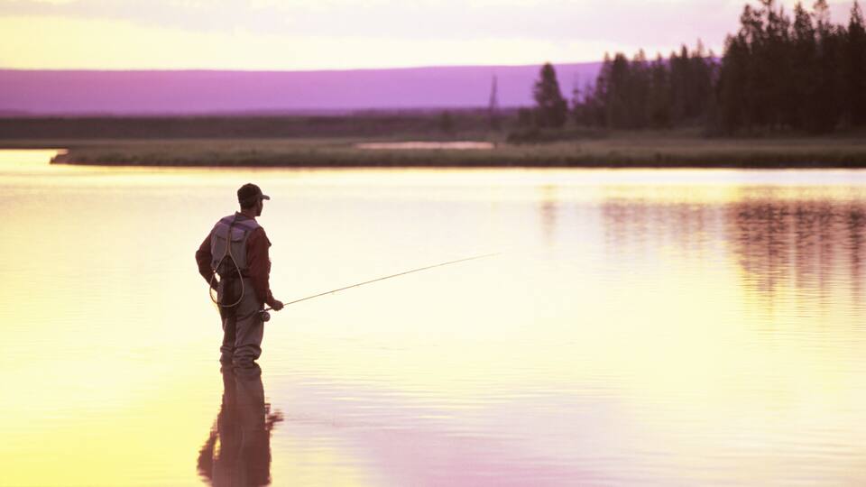 A person fishing by a calm lake at sunset.