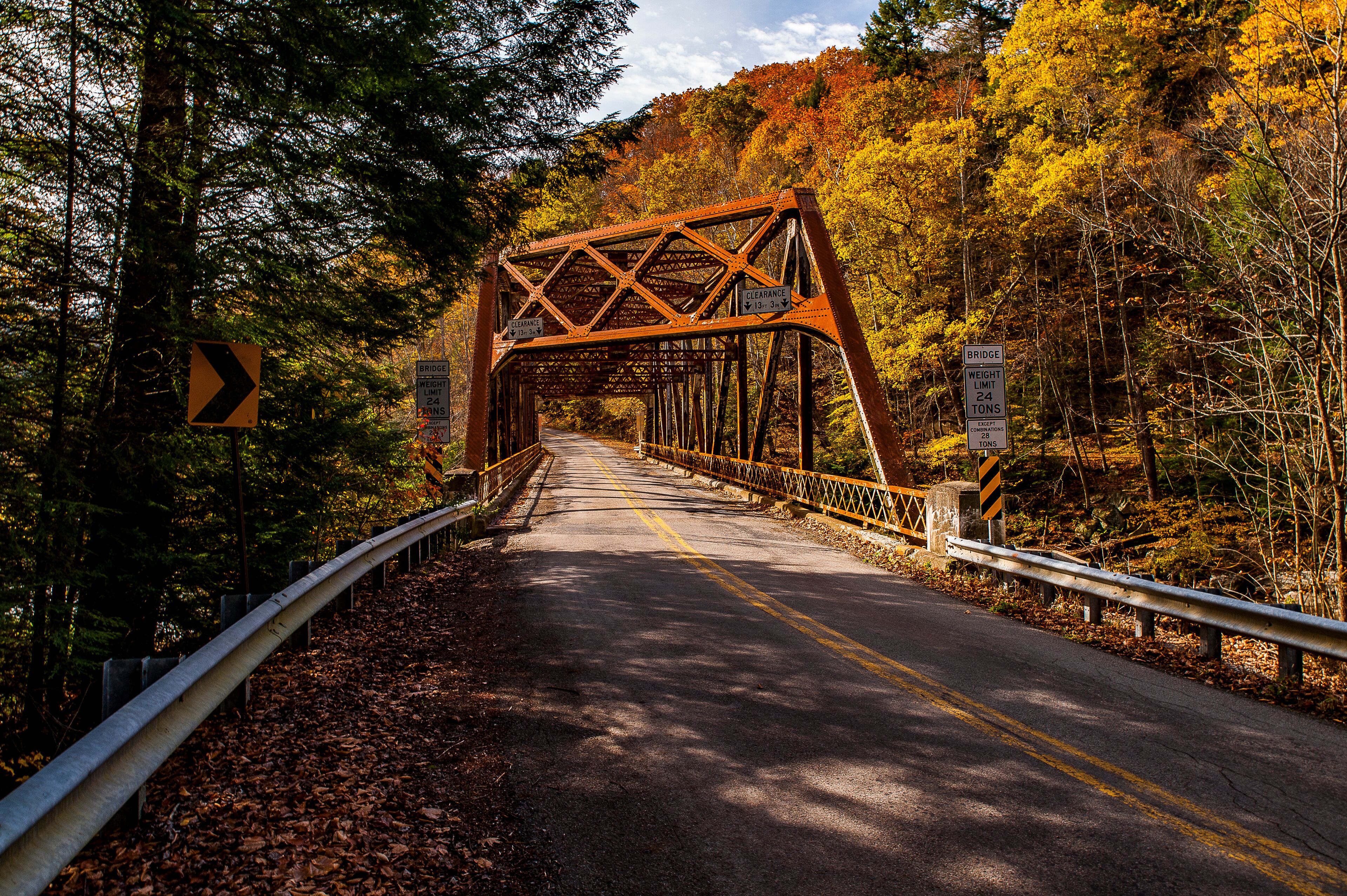 A steel bridge with a weight limit sign, surrounded by autumn foliage.
