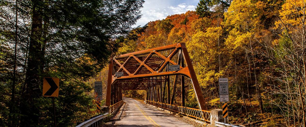 A steel bridge with a weight limit sign, surrounded by autumn foliage.