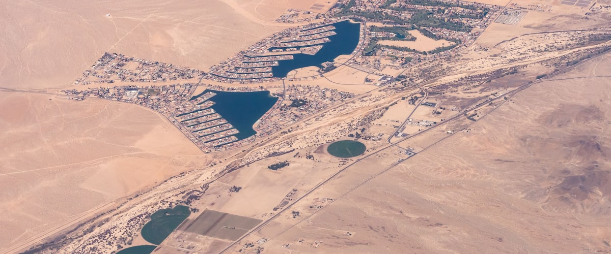 An aerial view of a desert landscape with a large water body, a dense cluster of buildings, and surrounding arid terrain.
