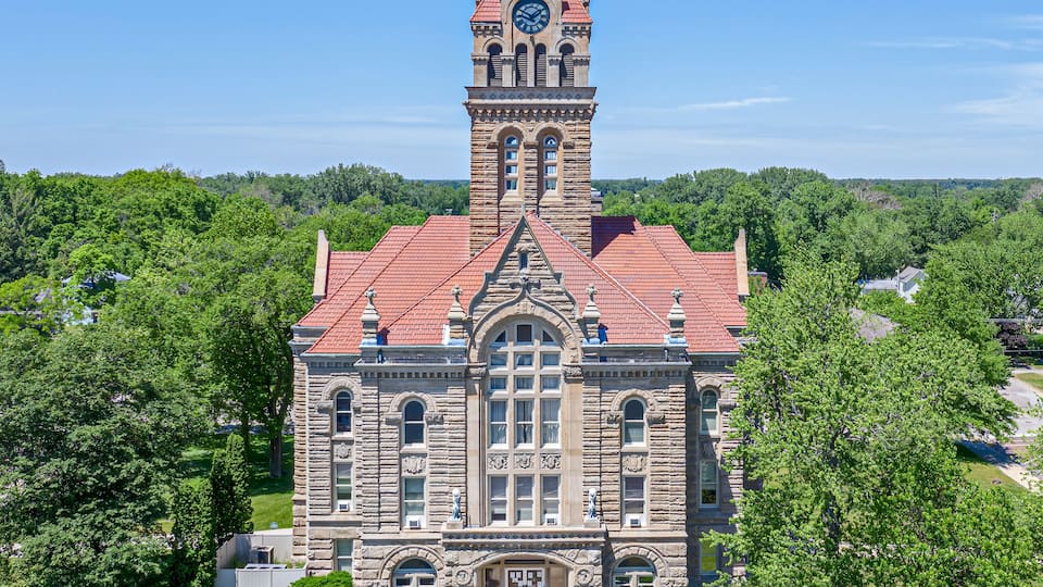 A large stone building with a clock tower, surrounded by lush greenery.