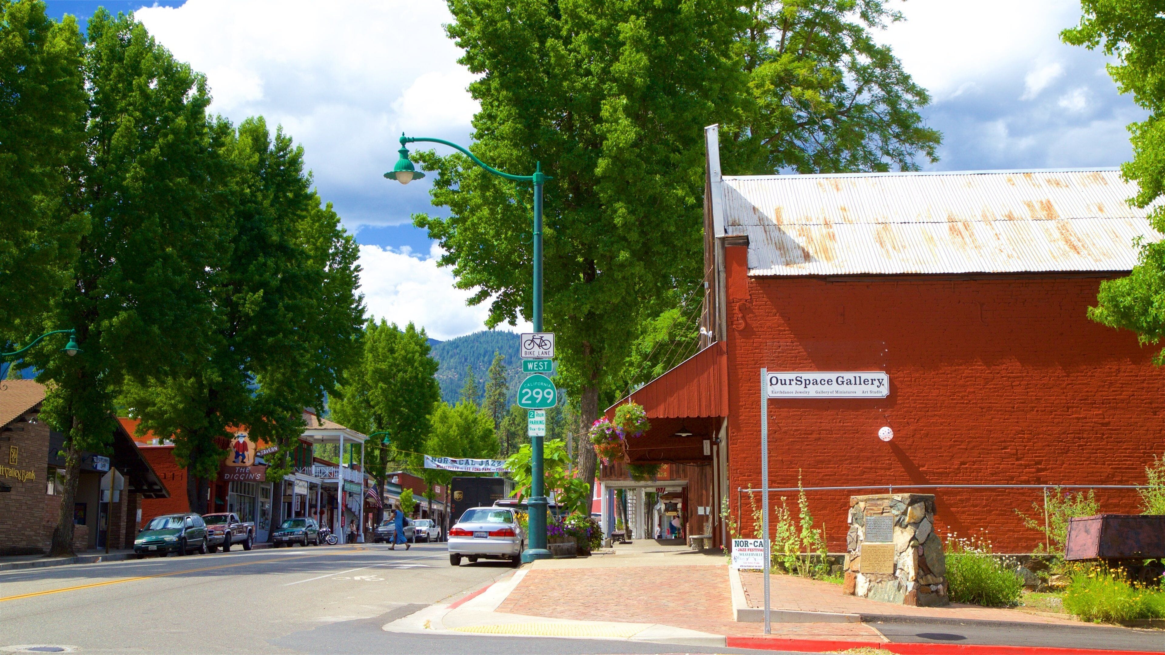 A street with a red brick building labeled "Our Space Gallery," a bike lane sign, and a mountain in the background.