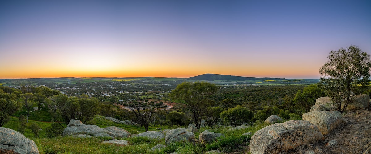 A landscape with rolling hills, scattered trees, and large boulders under a sunset sky.