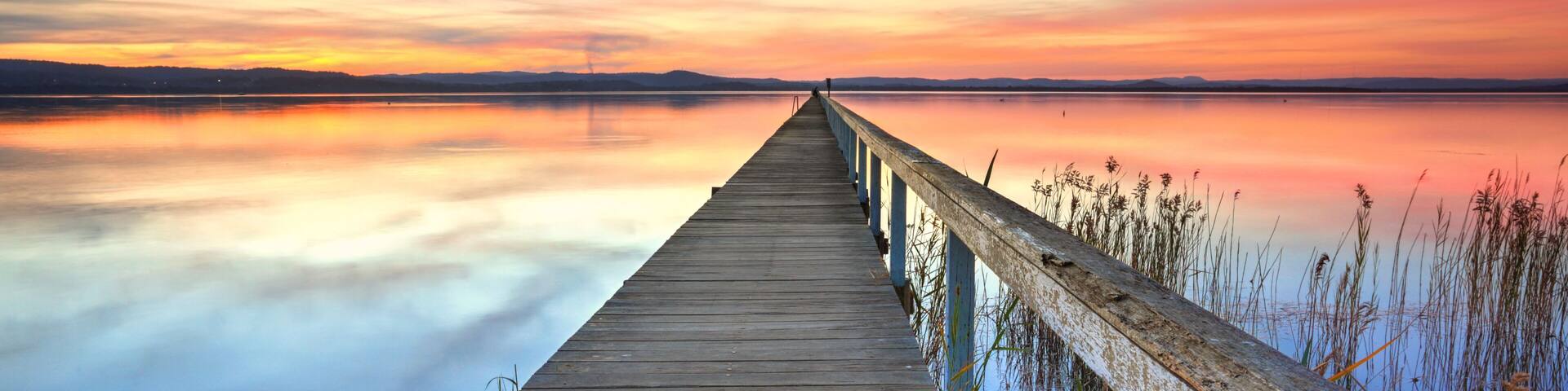 A wooden pier extending into a calm body of water with a sunset sky.