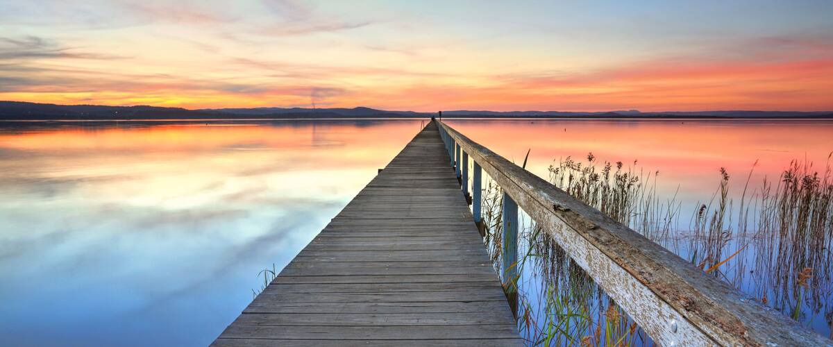 A wooden pier extending into a calm body of water with a sunset sky.