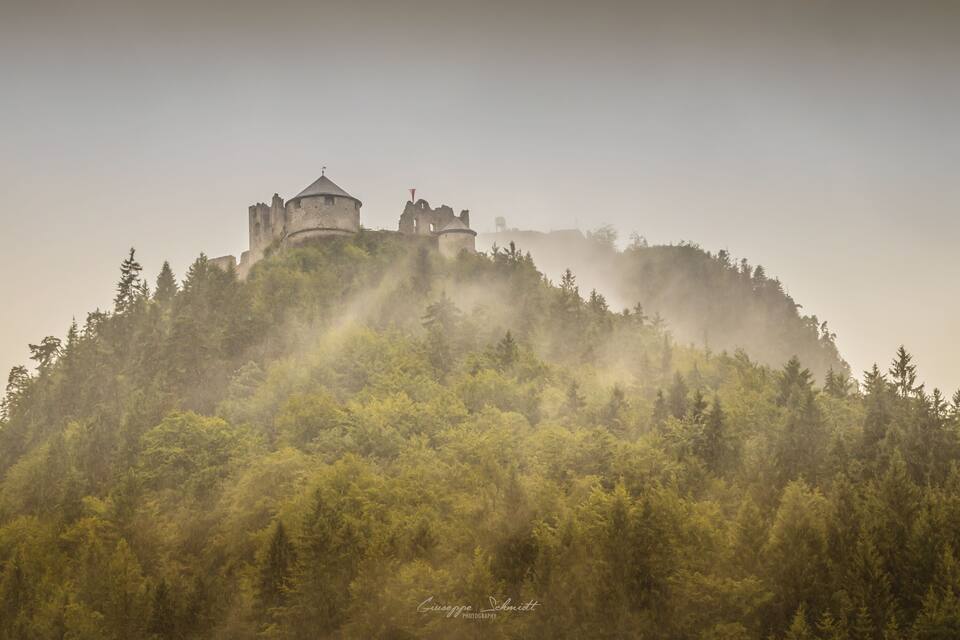 Um castelo numa colina enevoada com uma floresta densa.