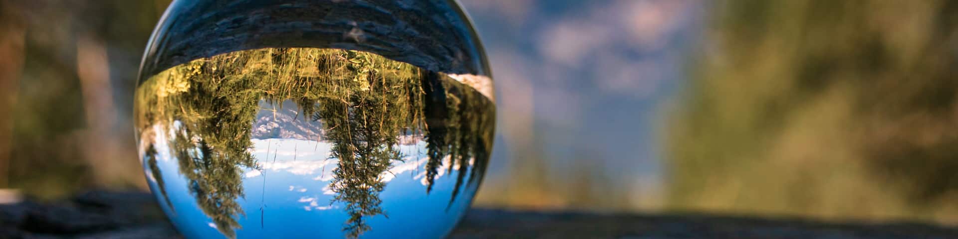 A reflective glass sphere on a wooden surface with a blurred natural background.