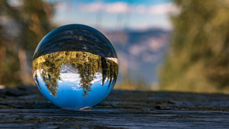 A reflective glass sphere on a wooden surface with a blurred natural background.