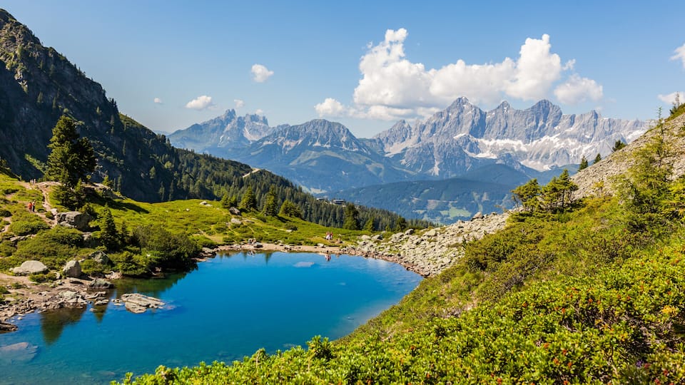 A mountain lake surrounded by lush greenery and towering peaks.