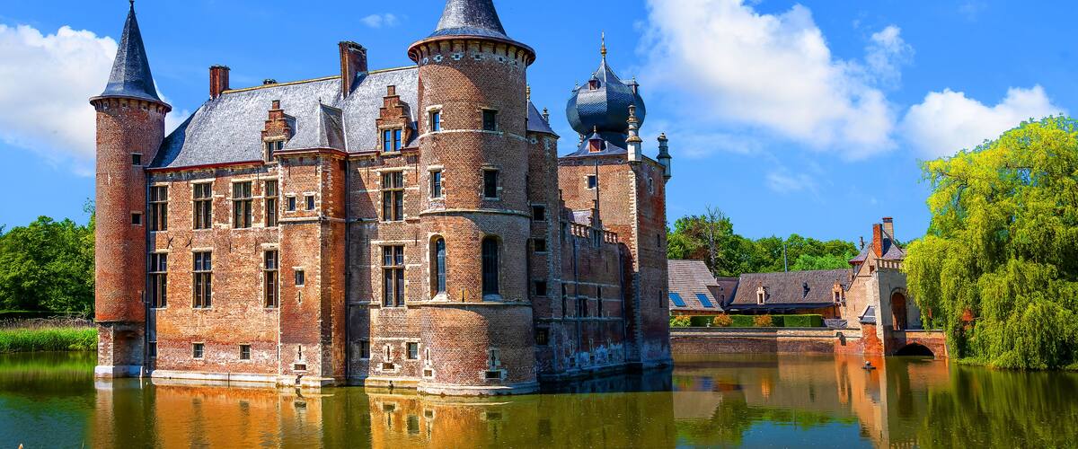 A historic castle with multiple towers and domes, situated by a calm river.