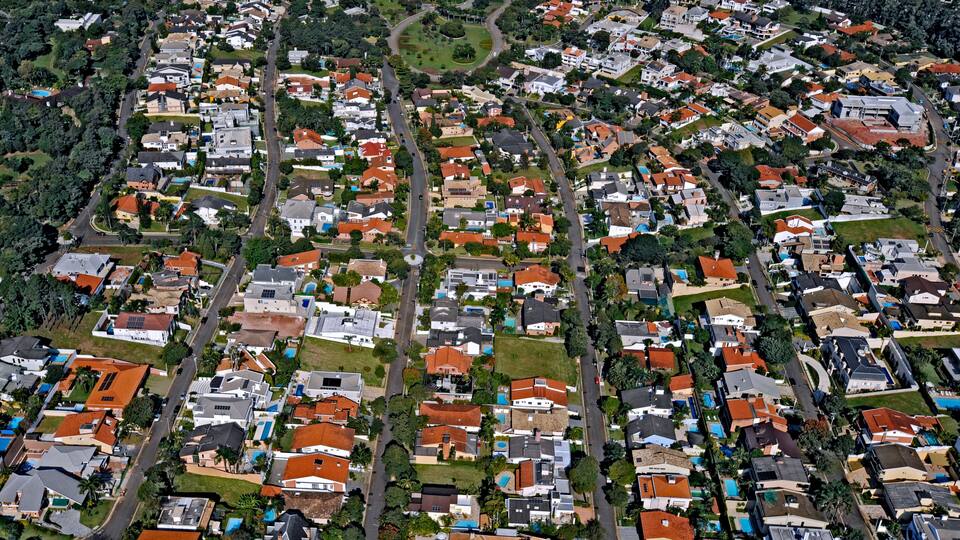 A densely packed residential area with a mix of single and multi-story houses, surrounded by greenery and intersecting roads.