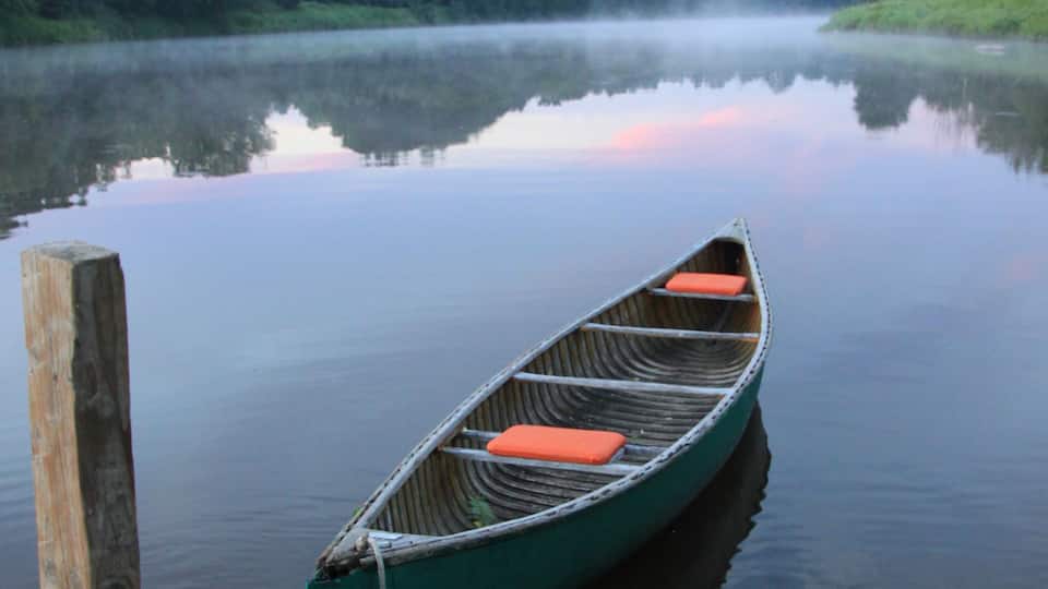 A canoe tied to a dock on a calm lake with a forest in the background.