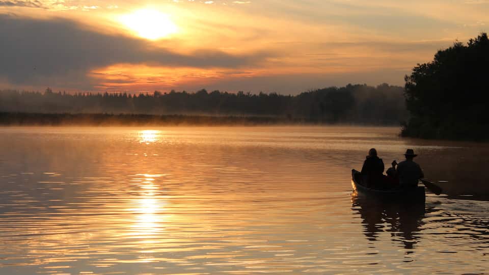 A sunset over a calm lake with a boat carrying people.