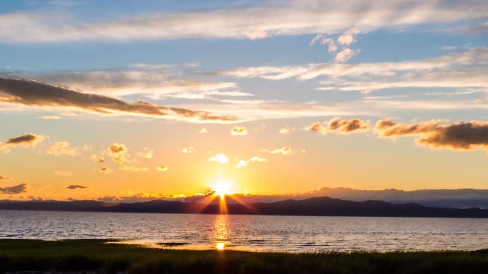 A sunset over a body of water with mountains in the distance.