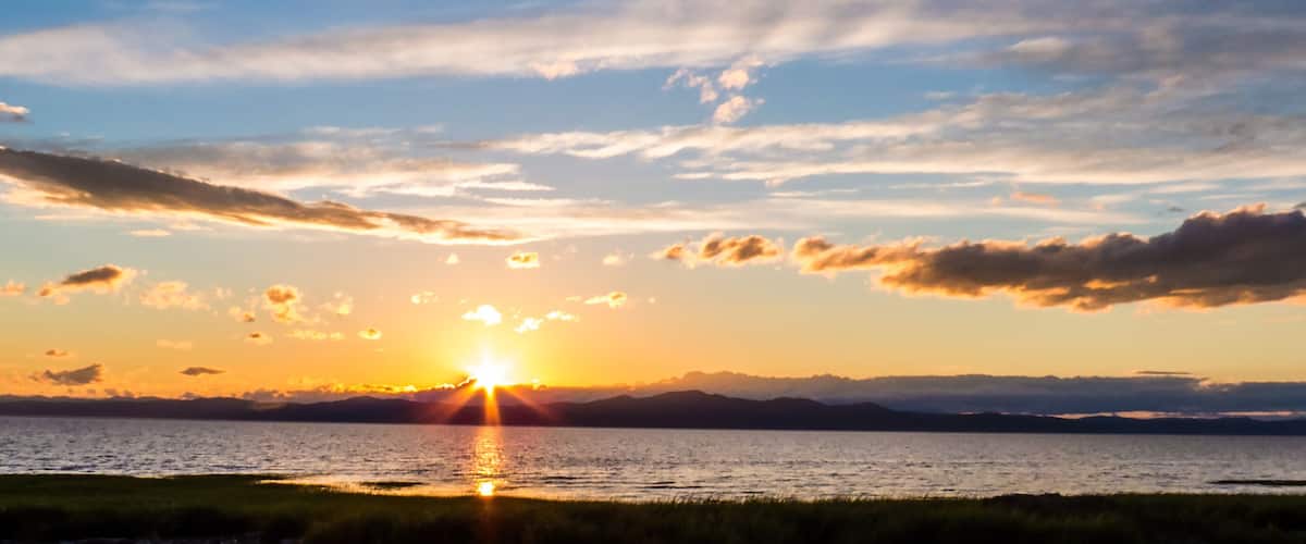 A sunset over a body of water with mountains in the distance.