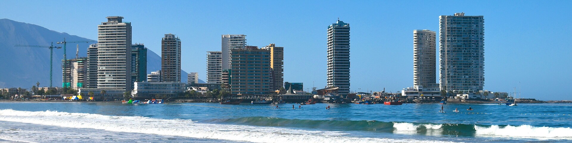 Una playa con olas y un horizonte urbano al fondo.