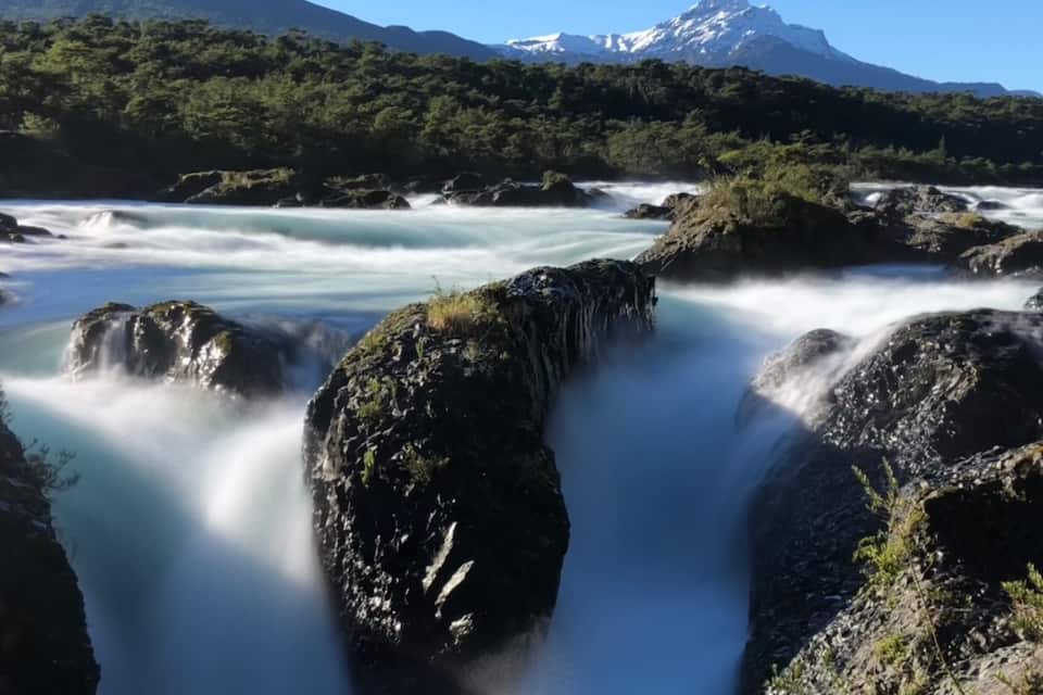 A waterfall cascading over rocks with a mountain in the background.