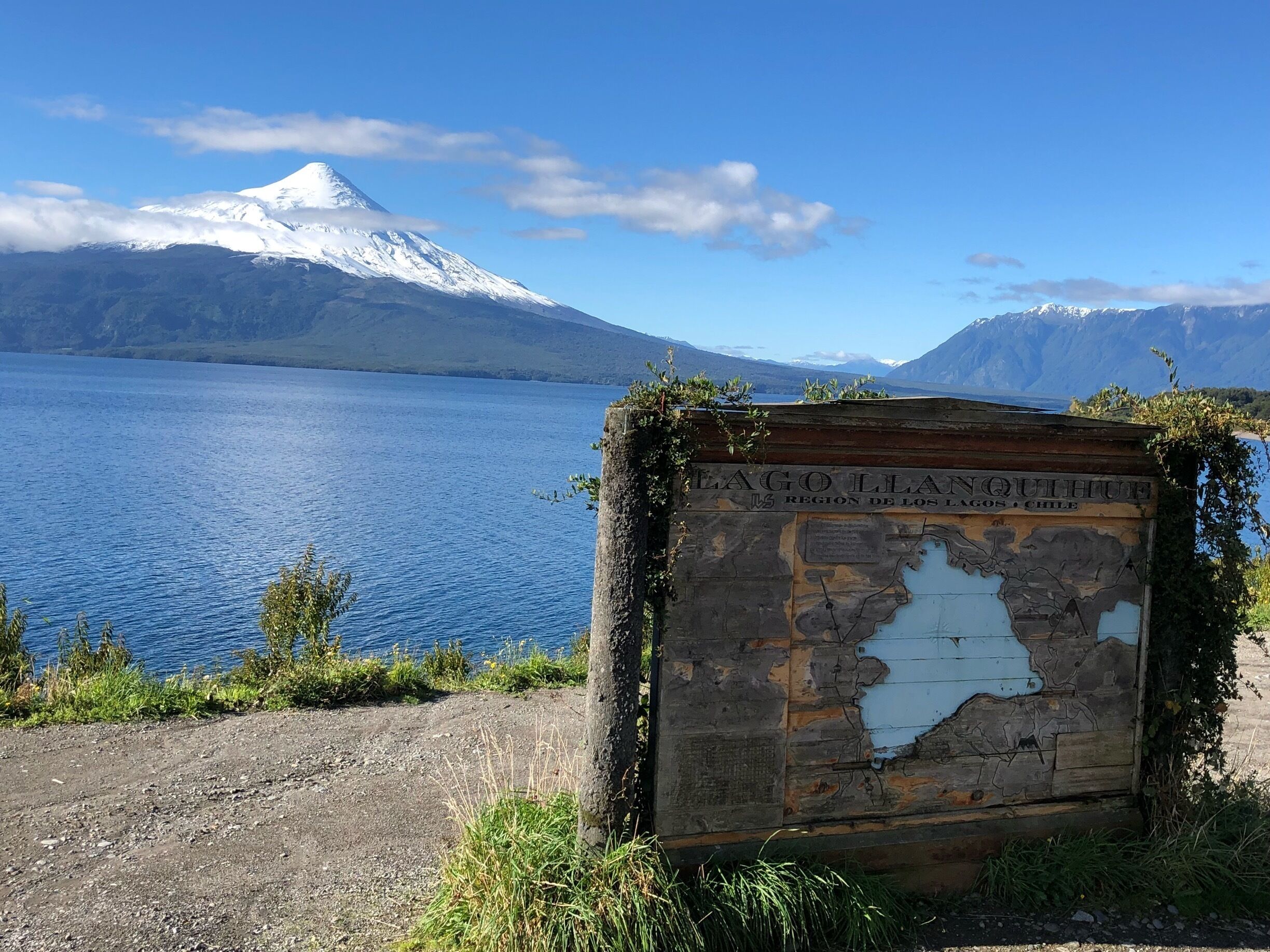 Un cartel con el texto 'LAGO LLA' y 'REGIÓN DE LOS LAGOS, CHILE', una montaña nevada y un lago tranquilo.