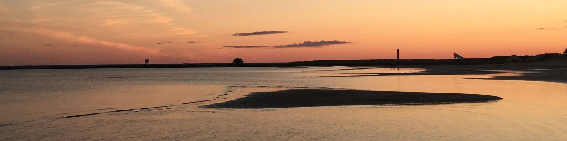 A calm beach at sunset with gentle waves and a clear sky.