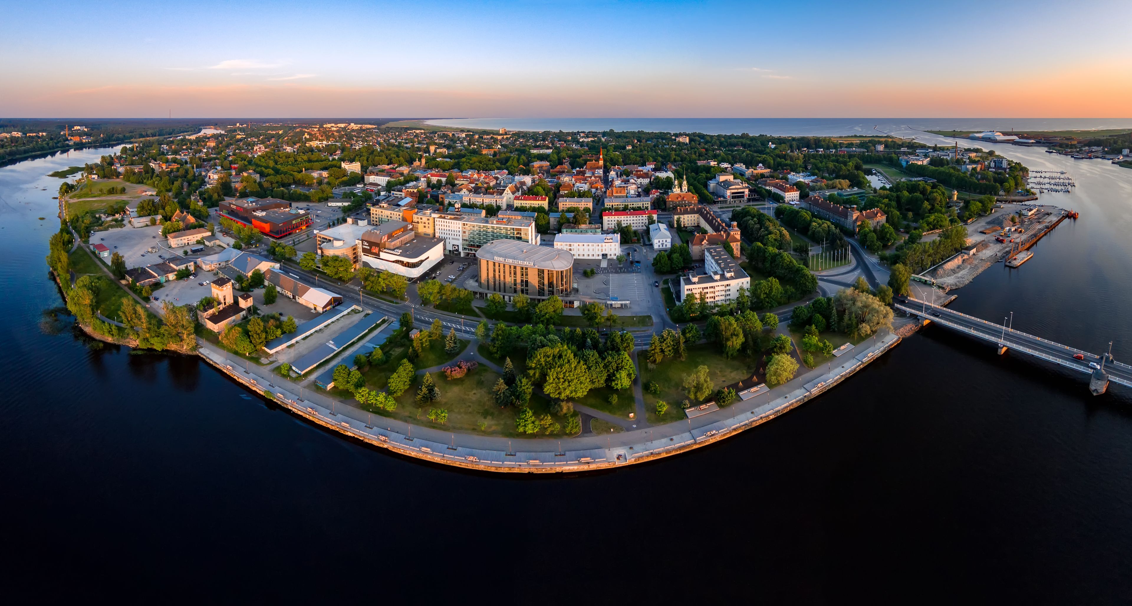 An aerial view of a coastal city with a prominent round building, a river, and a bridge.
