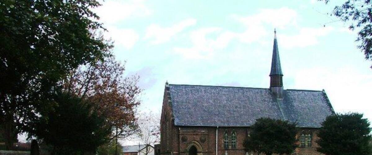 A church with a tall steeple, surrounded by a grassy area with trees and a stone wall.