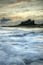 A castle on a cliff overlooking the ocean with waves crashing below.