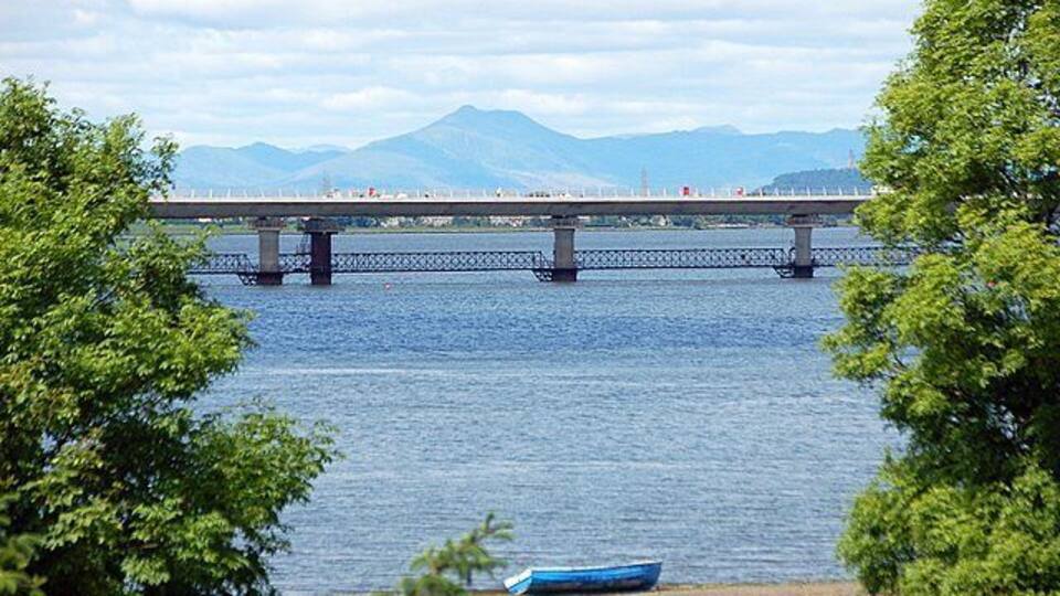 Un puente sobre un río, con montañas al fondo y un bote en la orilla.