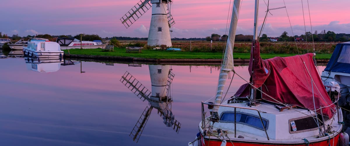 A windmill, boats, calm water, and a sunset sky.