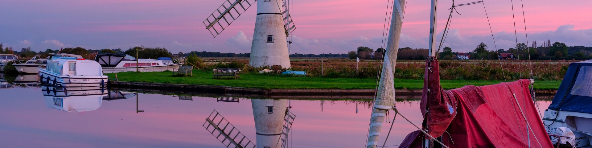 A windmill, boats, calm water, and a sunset sky.