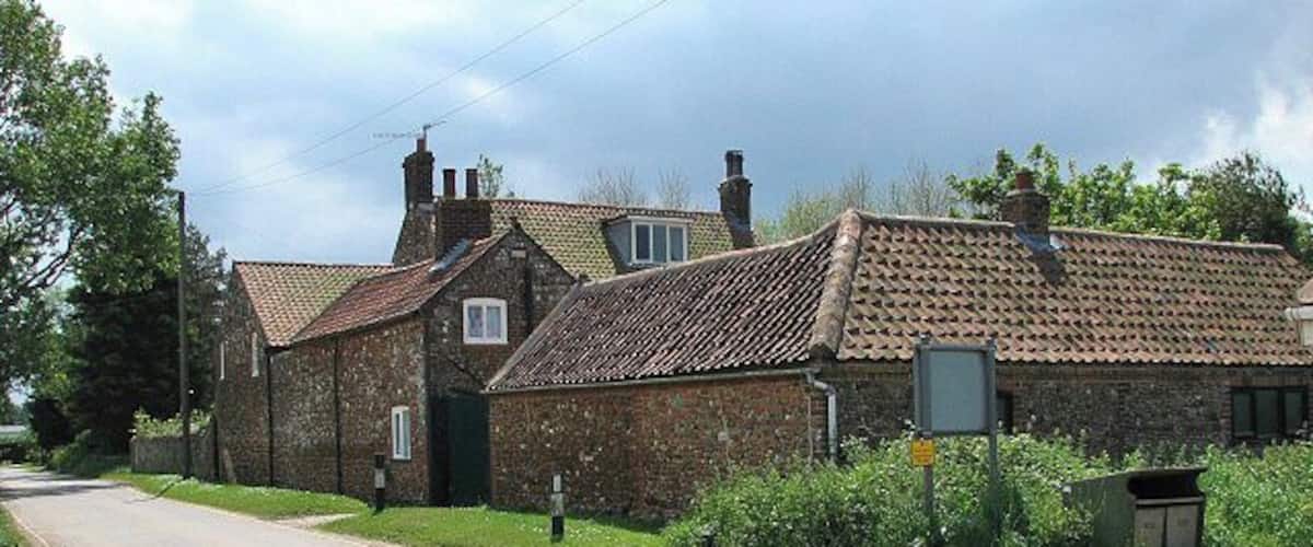 A rural road with stone houses, a clear sky, and a signpost.