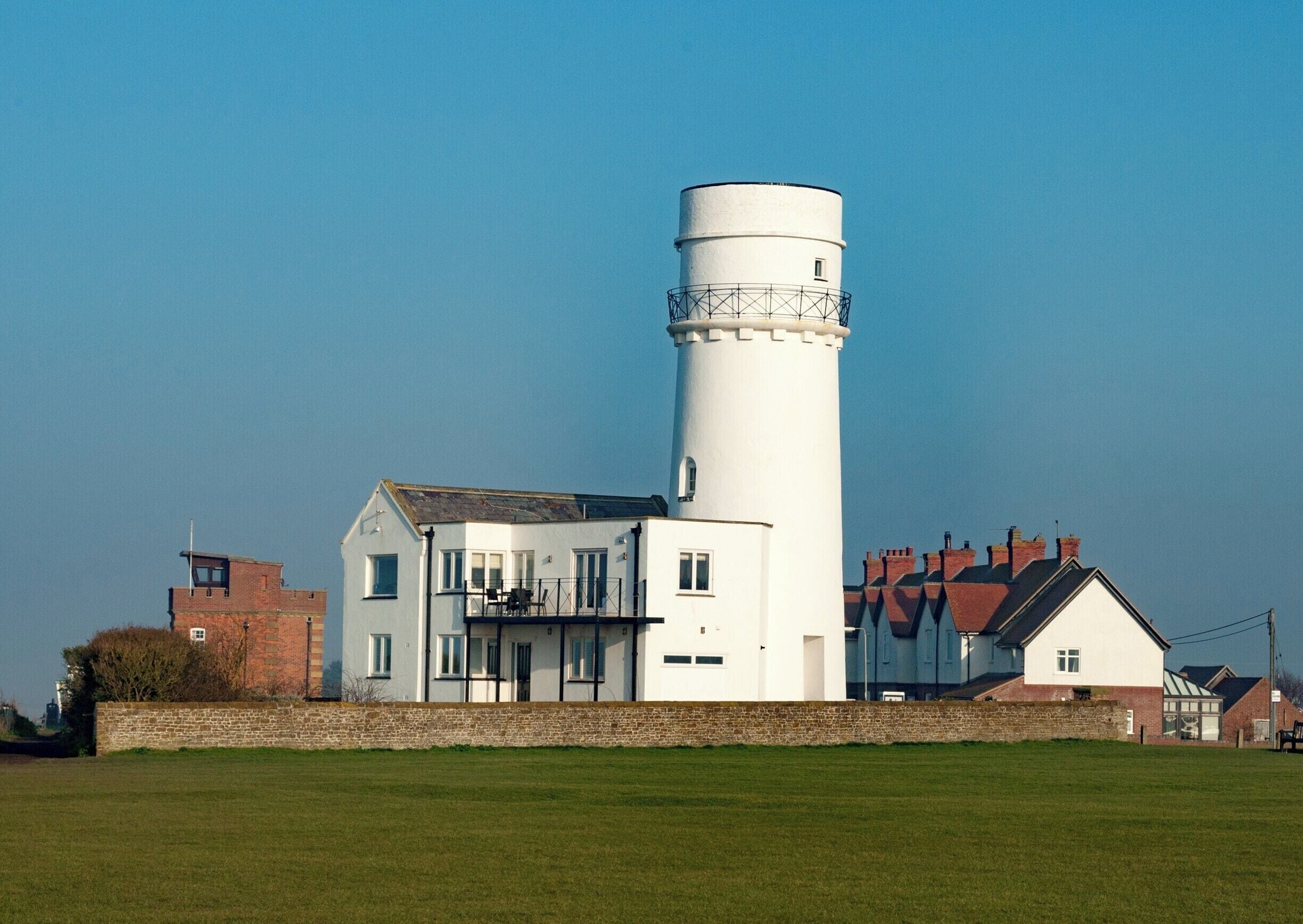 A white lighthouse with a cylindrical tower, a white building with a balcony, and a brick building with red roofs.